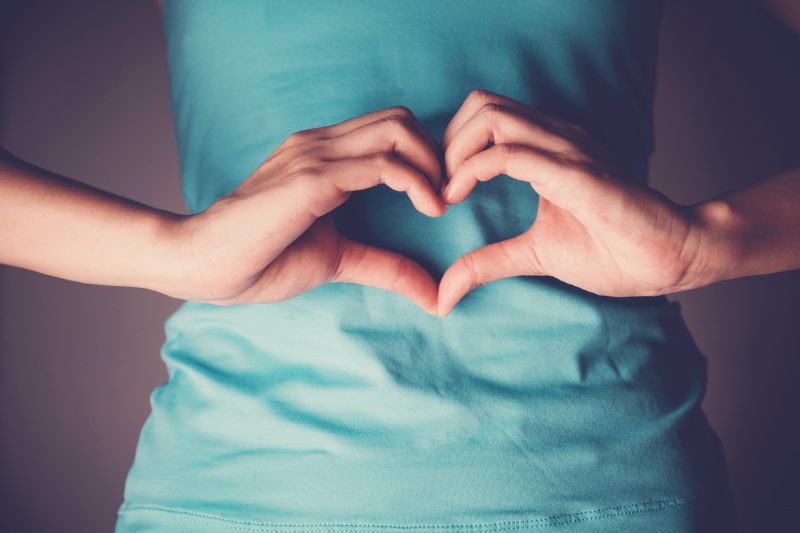 Woman hands making a heart shape on her stomach