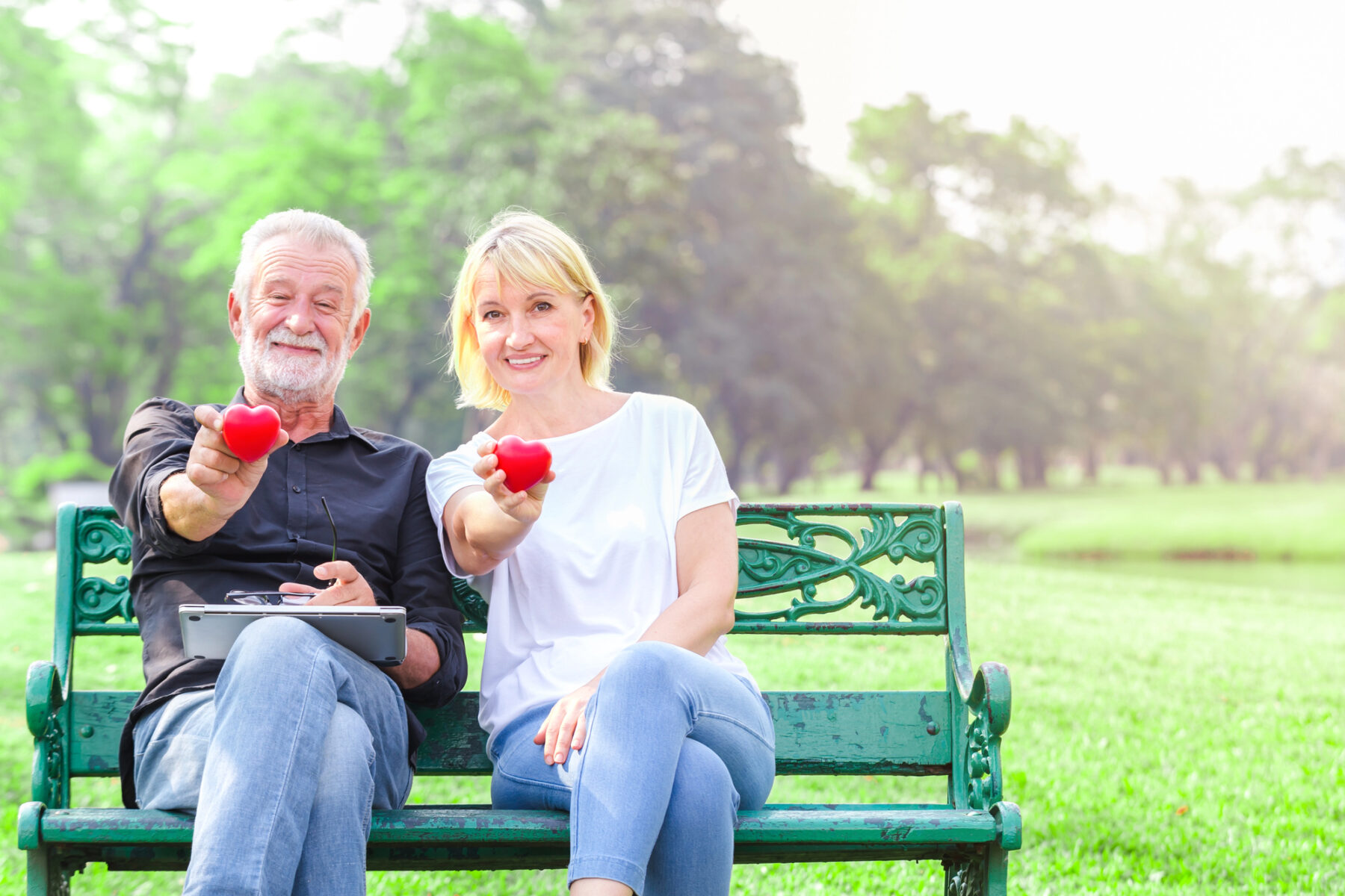 Healthy middle aged couple holding hearts on a park bench